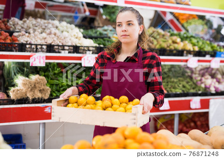 Young smiling woman salesman carrying box with yellow plums Young smiling woman salesman carrying box with yellow plums 76871248