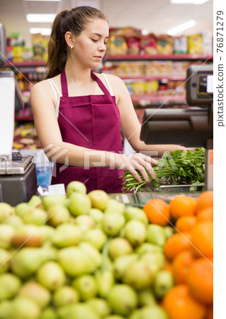 Young saleswoman weighs greens on a scale Young saleswoman weighs greens on a scale 76871279