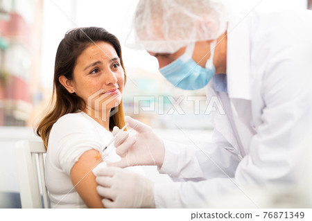 Man doctor in in protective mask making injection of vaccine to woman patient Man doctor in in protective mask making injection of vaccine to woman patient 76871349