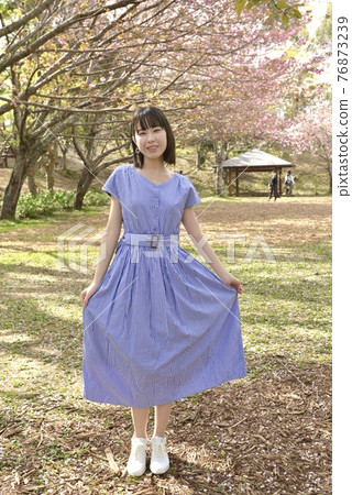 擺在櫻花公園的一位年輕、苗條的微笑婦女 76873239