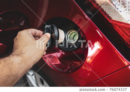 Human hand is open or close fuel tank cap of the red car for refueling Human hand is open or close fuel tank cap of the red car for refueling 76874337