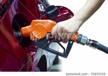 Hand holding pump nozzle is refueling into the fuel tank of a red car 76874339