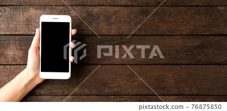 Woman hand holding smart phone with blank screen. Wooden background. Banner 76875850