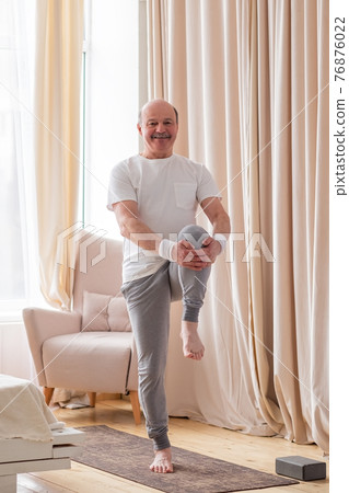 Senior handsome sportman doing stretching and balancing yoga exercise at home Senior handsome sportman doing stretching and balancing yoga exercise at home 76876022