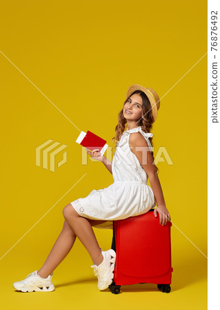 girl with passport and ticket sitting on red suitcase 76876492