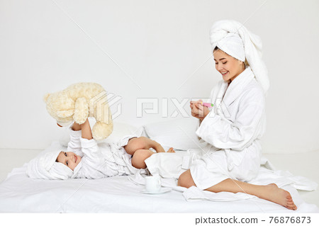 mother making manicure and daughter playing with teddy bear mother making manicure and daughter playing with teddy bear 76876873