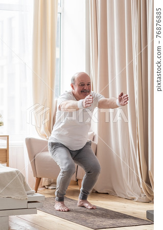 Senior man practicing yoga at home doing Chair pose, Utkatasana 76876885