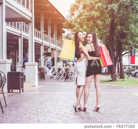 young Asia. Smiling women  with long beautiful hair on happy face in colorful white and black coats fashion makeup holding bags on street background 76877168