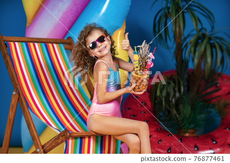 Smiling girl in swimsuit and sunglasses sitting in rainbow deck 76877461