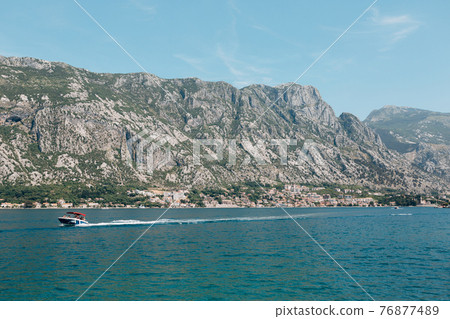 Motor boat with tourists on board sails along the Kotor bay against the backdrop of mountains Motor boat with tourists on board sails along the Kotor bay against the backdrop of mountains 76877489
