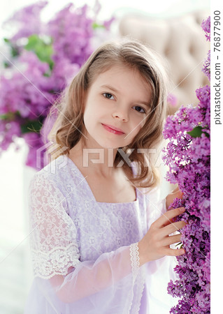 Beautiful little girl of preschool age in a delicate dress sitting on a swing decorated with flowers of lilac. 76877900