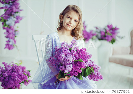 Beautiful little girl of preschool age in a delicate dress sitting on a swing decorated with flowers of lilac. 76877901