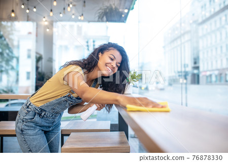 Young woman diligently wiping table surface Young woman diligently wiping table surface 76878330