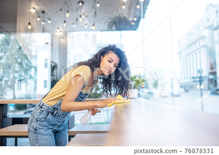 Serious looking woman wiping table clean in cafe Serious looking woman wiping table clean in cafe 76878331