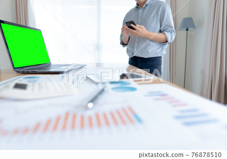 Businessman in casual wear stands beside desk to work at home with smartphone. work from home. Businessman in casual wear stands beside desk to work at home with smartphone. work from home. 76878510