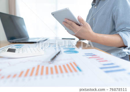 Businessman in casual wear stands beside desk to work at home with taplat. work from home. Businessman in casual wear stands beside desk to work at home with taplat. work from home. 76878511