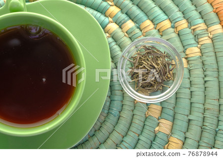 top view of green tea and herbal leaf in a small glass bowl on table  76878944