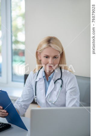 Woman doctor sitting in office looking at laptop 76879028