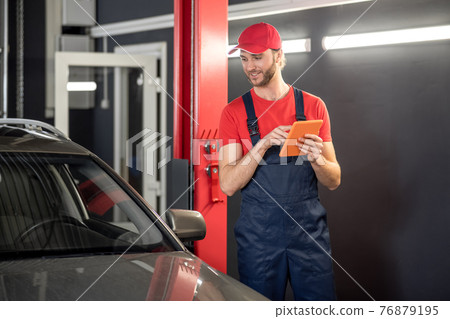 Man with tablet near car in workshop 76879195
