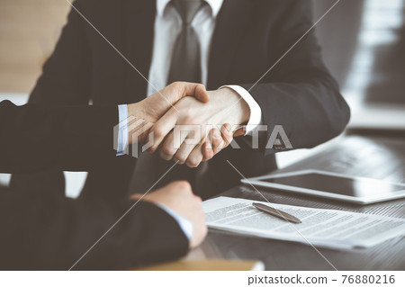 Unknown businessmen shaking hands above the glass desk in a modern office, close-up. Unknown business people at meeting. Teamwork, partnership and handshake concept 76880216