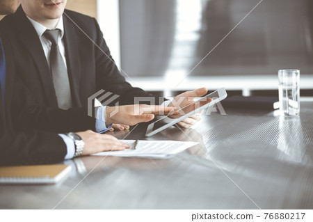 Unknown businessmen using tablet computer and work together at the glass desk in modern office, close-up. Teamwork and partnership concept Unknown businessmen using tablet computer and work together at the glass desk in modern office, close-up. Teamwork and partnership concept 76880217