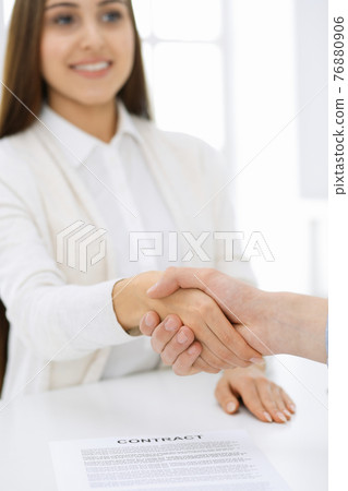 Casual dressed businessman and woman shaking hands after contract signing in white colored office. Handshake concept Casual dressed businessman and woman shaking hands after contract signing in white colored office. Handshake concept 76880906