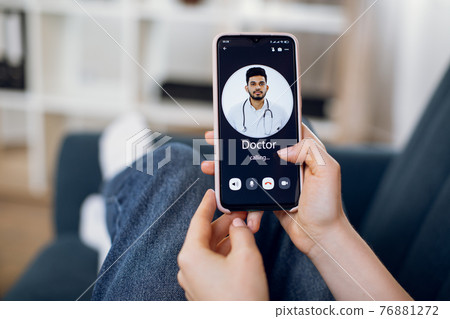 Close-up back view of female patient hands, using smart phone and calling to her doctor, young Indian man. App for remote medical service Close-up back view of female patient hands, using smart phone and calling to her doctor, young Indian man. App for remote medical service 76881272