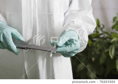 Worker In Protective Overalls Holding Calipers In Greenhouse Worker In Protective Overalls Holding Calipers In Greenhouse 76883984