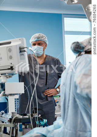 Anesthesiologist keeping track of vital functions of the body during cardiac surgery. Surgeon looking at medical monitor during surgery. Doctor checking monitor for patient health status. Anesthesiologist keeping track of vital functions of the body during cardiac surgery. Surgeon looking at medical monitor during surgery. Doctor checking monitor for patient health status. 76884268