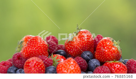 Pile od strawberries, blueberries, raspberries on green background 76885168