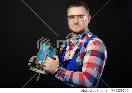 Portrait Caucasian man builder carpenter in a shirt and overalls with an electric tool in his hands. Studio portrait of friendly artisan businessman 76885495