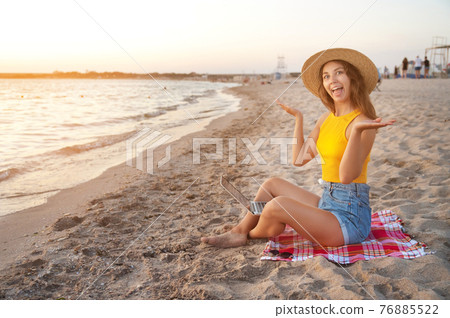 young happy crazy attractive caucasian woman freelancer, wearing a hat, sitting on a sandy beach by the sea with a laptop on her laptop young happy crazy attractive caucasian woman freelancer, wearing a hat, sitting on a sandy beach by the sea with a laptop on her laptop 76885522