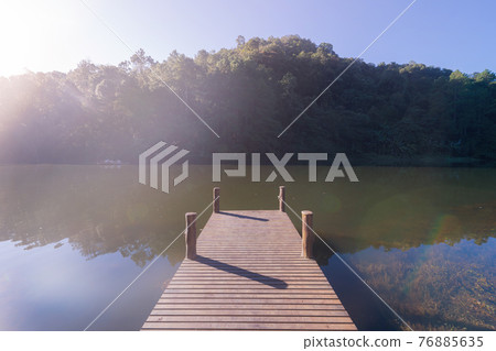 Wooden bridge pier with lake and forest trees in Pang Ung reservoir, Mae Hong Son, Thailand. Tourist attraction, surrounded by green pine, mountains, reflection from water. Wooden bridge pier with lake and forest trees in Pang Ung reservoir, Mae Hong Son, Thailand. Tourist attraction, surrounded by green pine, mountains, reflection from water. 76885635