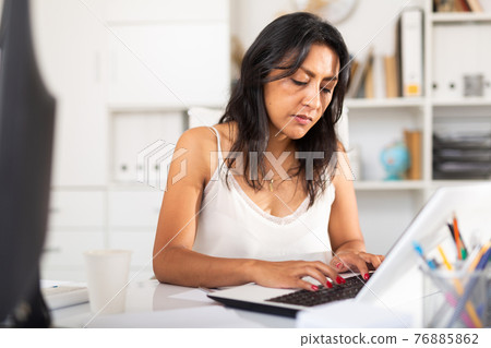Busy female entrepreneur in office with papers and laptop 76885862
