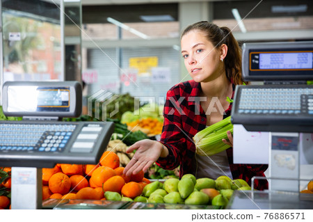Young female customer holds celery in her hands and chooses tangerines 76886571