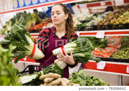Portrait of a young saleswoman laying out bundles of chinese cabbage on the counter 76886642
