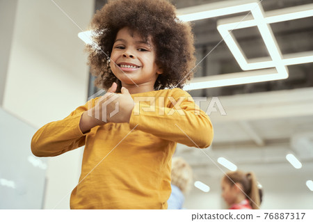 Portrait of joyful little boy smiling at camera while posing in a classroom 76887317