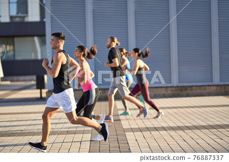 Men and women in sports clothing jogging outdoors 76887337