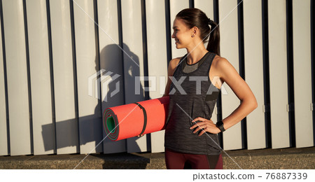 Happy beautiful woman holding exercise mat outdoors 76887339
