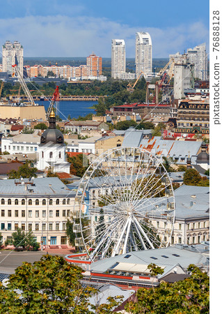 Ferris wheel and bell tower with copper roof and gilded dome in the old Podil district in Kyiv, cityscape on a summer day. Ferris wheel and bell tower with copper roof and gilded dome in the old Podil district in Kyiv, cityscape on a summer day. 76888128