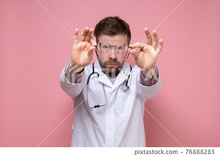 Serious doctor has taken off glasses, keeps them away from face trying to see something, and looks 76888283