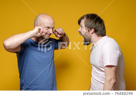 Two men, one in a rage screams loudly at the other who covered his ears with his fingers and looks Two men, one in a rage screams loudly at the other who covered his ears with his fingers and looks 76888299