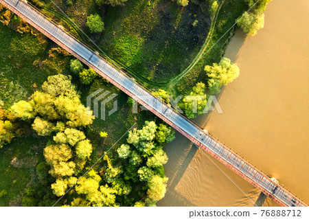 Aerial view of a narrow road bridge stretching over muddy wide river in green rural area. Aerial view of a narrow road bridge stretching over muddy wide river in green rural area. 76888712