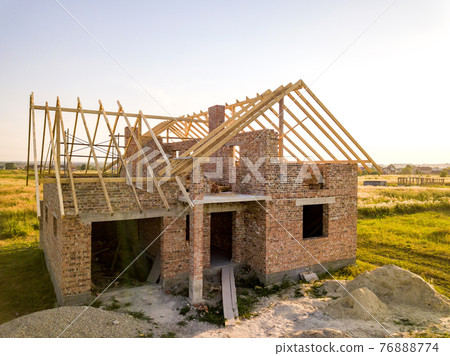 Unfinished brick house with wooden roof structure under construction. Unfinished brick house with wooden roof structure under construction. 76888774