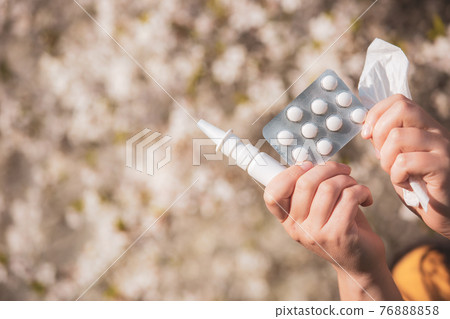 Allergy concept, young woman with pills or drugs and nose or nasal spray against the strong allergy in hand in front of blooming a tree during spring season, healthcare 76888858