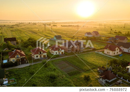 Aerial view of rural residential area with private homes between green fields at sunrise. Aerial view of rural residential area with private homes between green fields at sunrise. 76888972