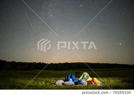 People resting in night field observing dark sky with many bright stars. People resting in night field observing dark sky with many bright stars. 76889100