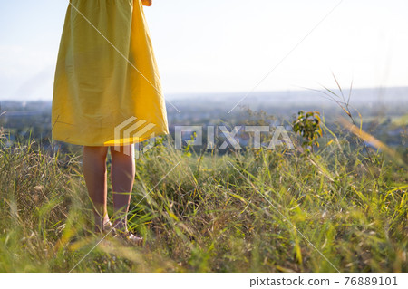 Close up of young woman legs in yellow summer dress standing in grassy field outdoors. 76889101