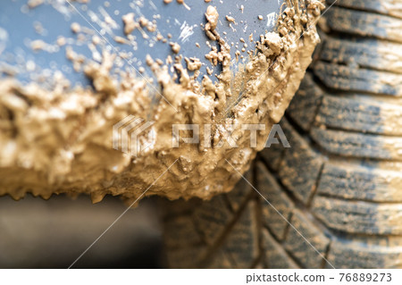 Close up of dirty car wheel with rubber tire covered with yellow mud. Close up of dirty car wheel with rubber tire covered with yellow mud. 76889273