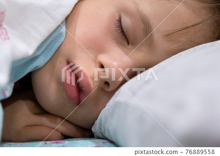 Close up of a face of pretty little child girl with slightly open mouth and scattered around hair sleeping in bed at home. 76889558